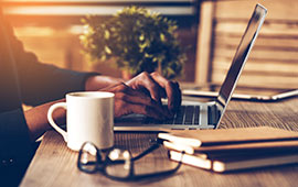 Man sitting at desk with laptop, glasses and coffee.